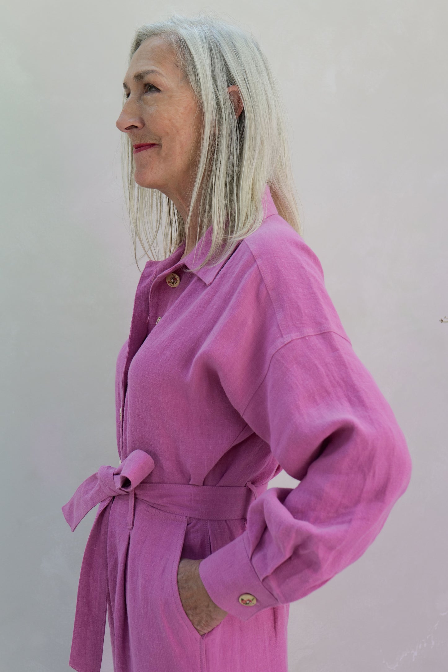 Woman wearing a pink linen jumpsuit against a plain background