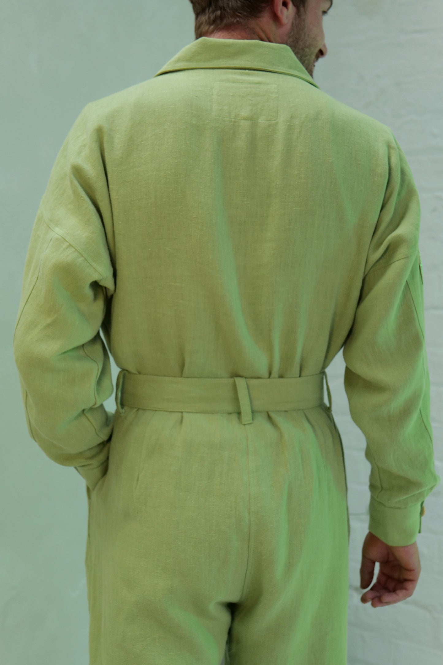 Person wearing a light green linen jumpsuit against a plain background