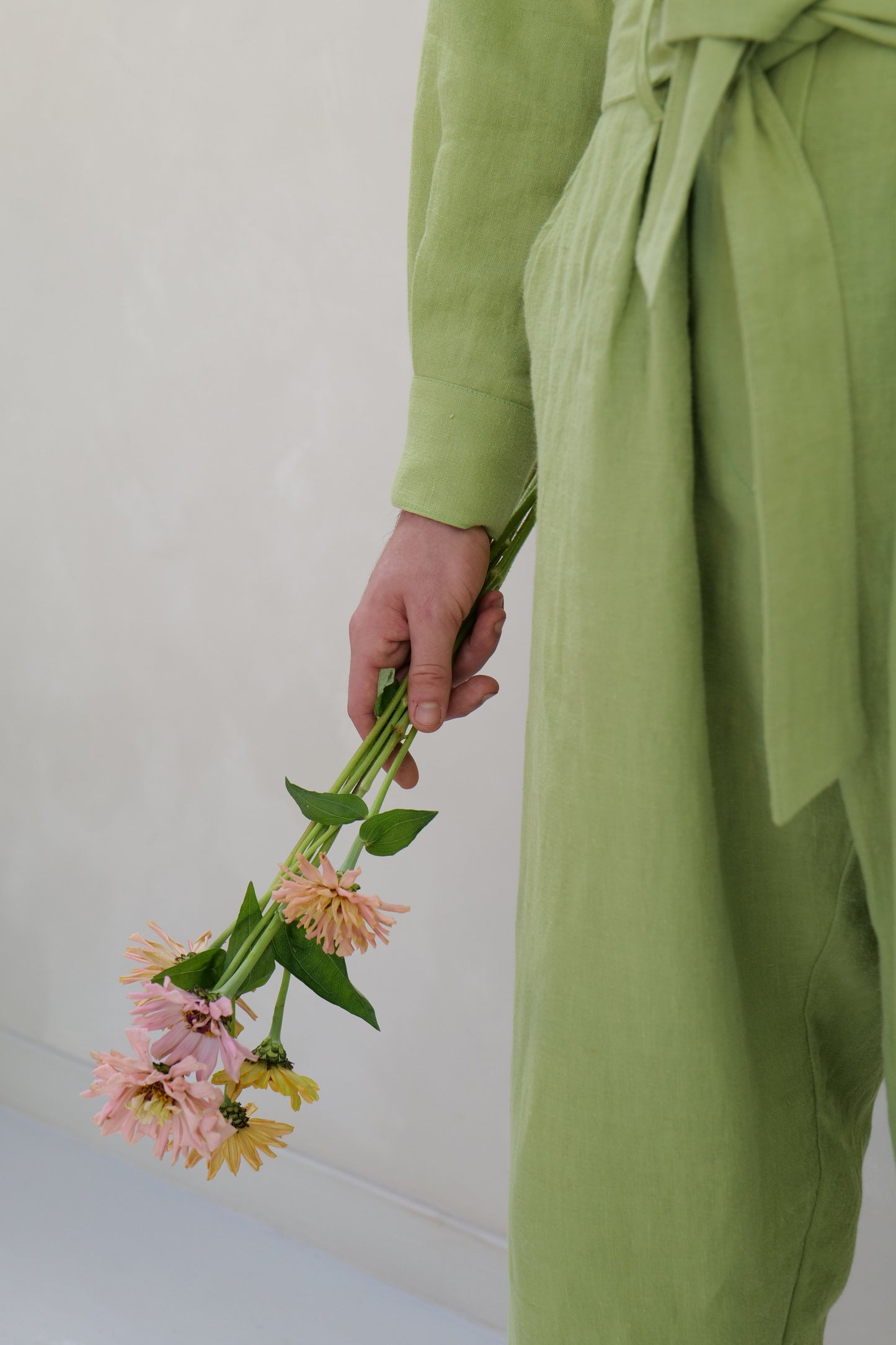 Person wearing a green linen outfit holding a bouquet of flowers against a plain background
